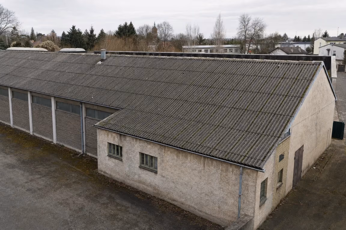 Flach geneigtes Dach eines älteren Gewerbebaus mit grauen Faserzement-Wellplatten, Bemoosung in den Wellentälern und sichtbaren Plattenüberlappungen
