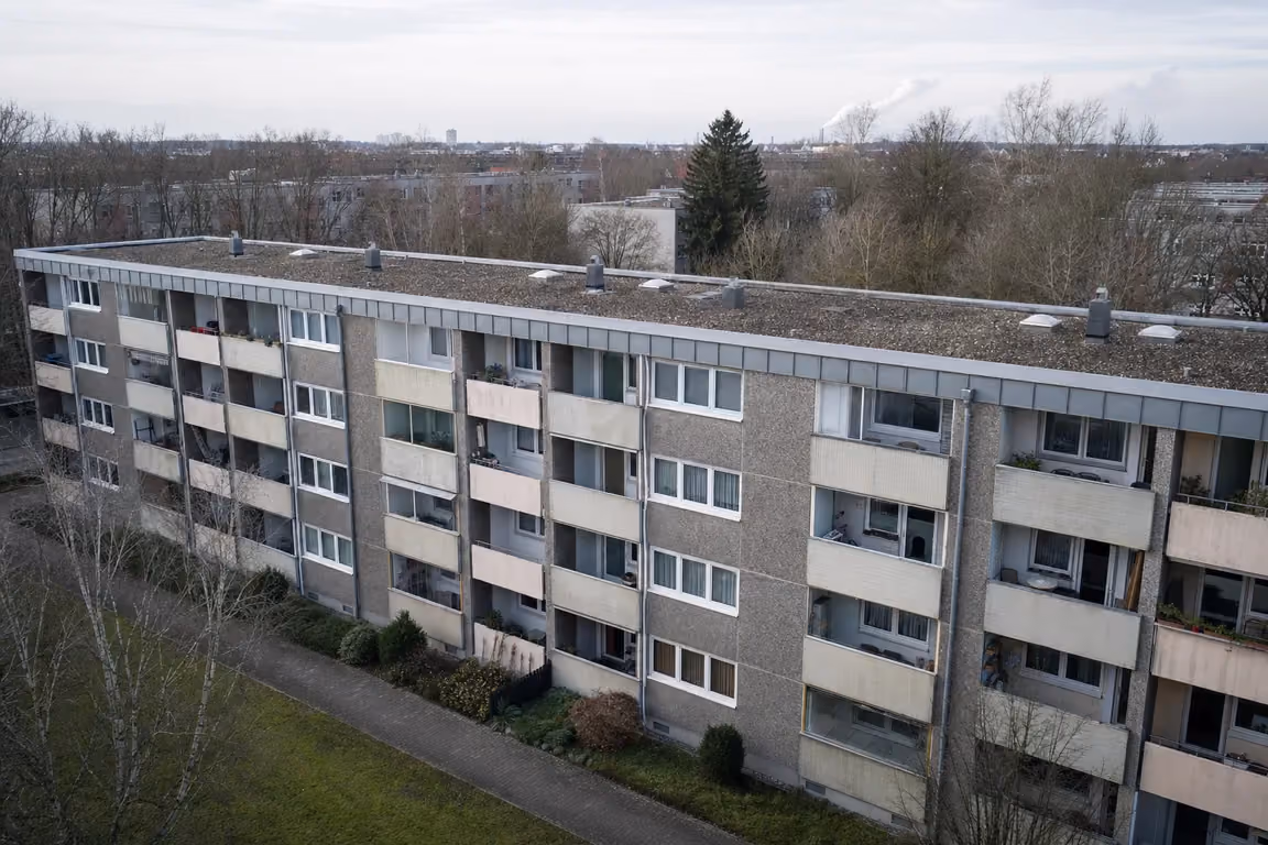 Dachwartung für die Wohnungswirtschaft: Mehrfamilienhaus-Zeile von der Balkonseite, darüber das bekieste Flachdach mit Lichtkuppeln, Entlüftern und Attika-Abdeckung