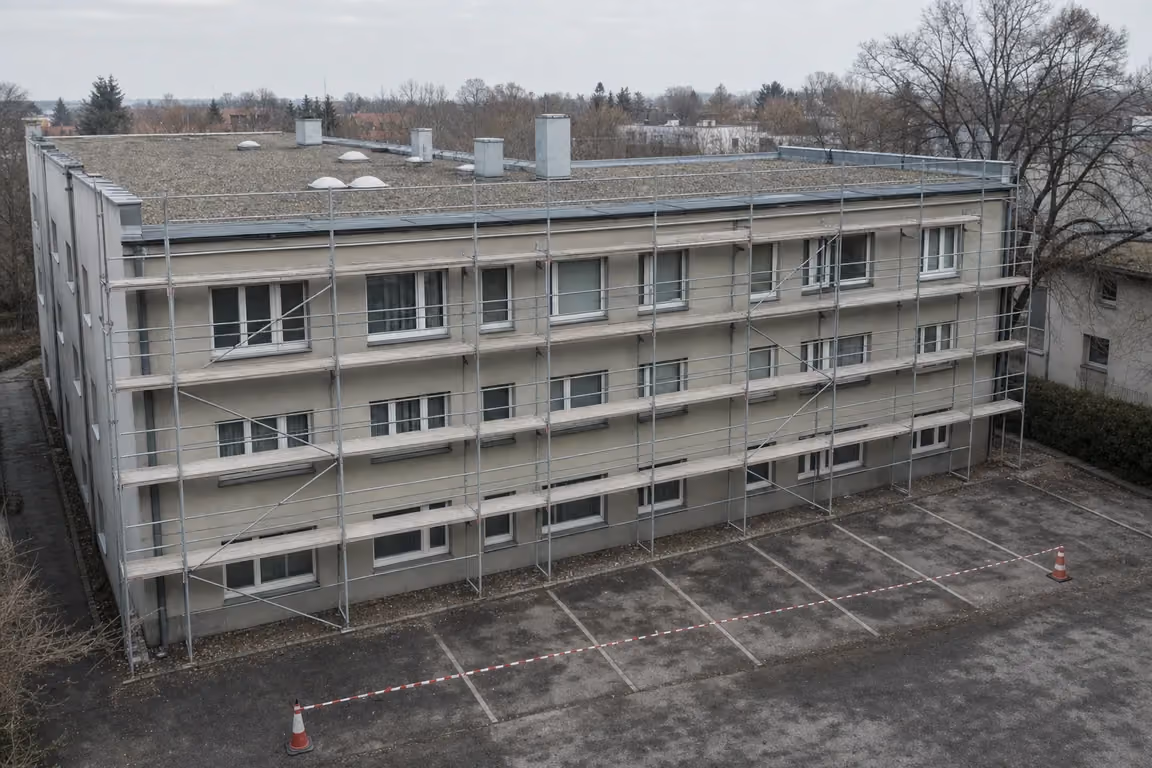 Wohngebäude mit Fassadengerüst über der Traufe, davor mit Absperrband und Leitkegeln gesperrte Stellplätze