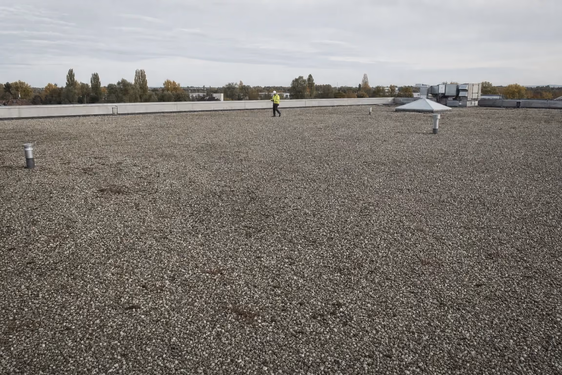Flachdach vor der PV-Belegung prüfen: Techniker geht bei der Begehung die noch leere Kiesdachfläche ab