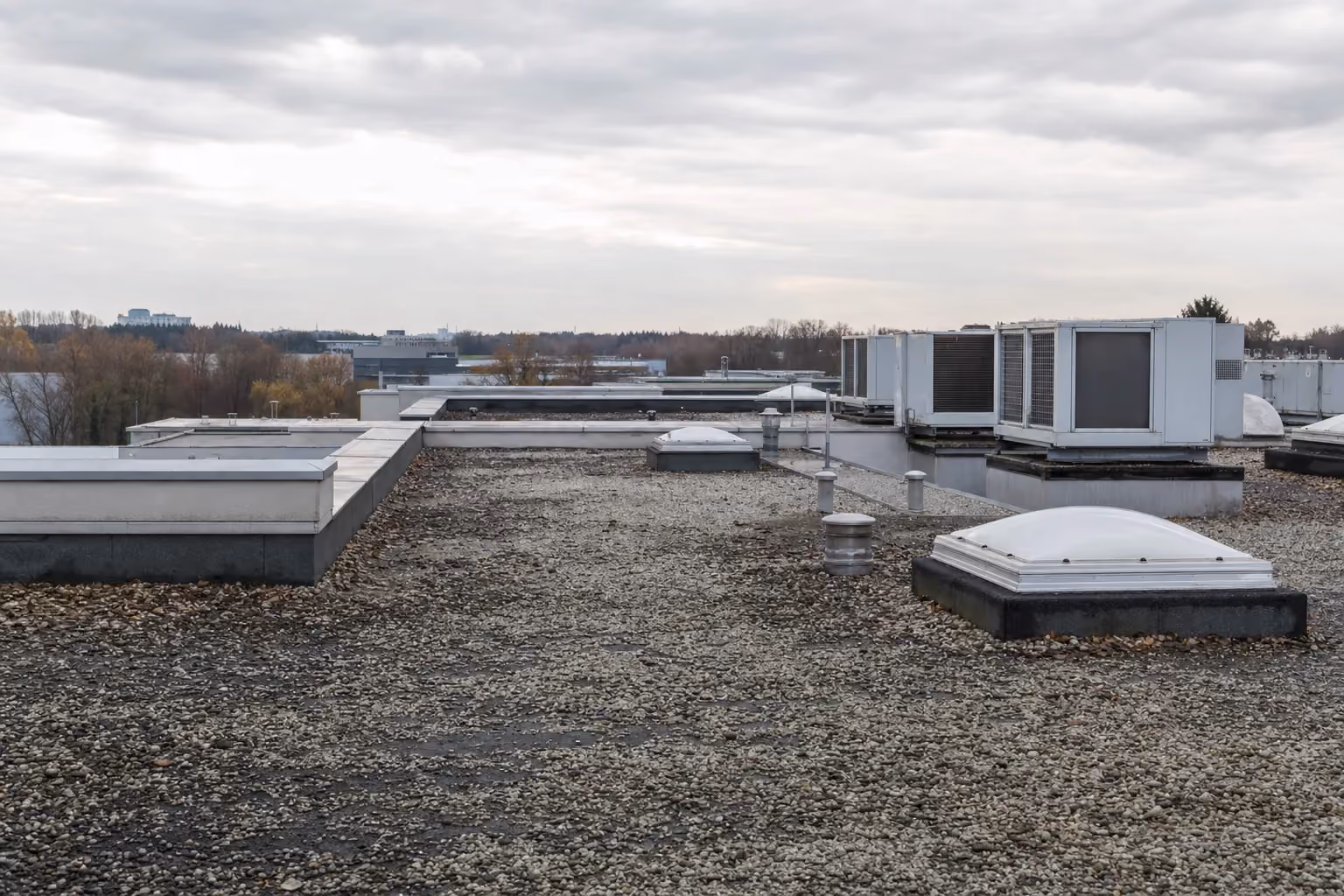 Mehrere aneinandergrenzende gewerbliche Flachdächer auf leicht unterschiedlichen Höhen mit Lüftungsaggregaten, Lichtkuppel und Entlüftern über Kiesschüttung